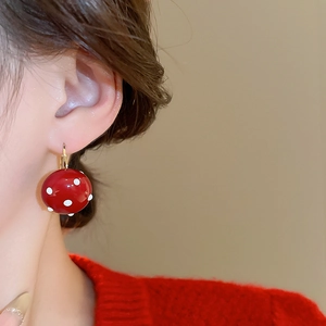 Close-up of a model wearing a red pearl sphere earring with white polka dots and gold hook