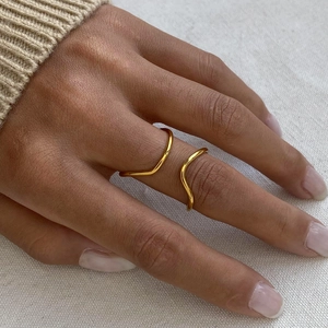 Close-up of a minimalist gold wave-shaped open ring worn on a finger with knitwear background
