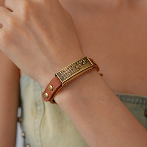 Detail of vintage brown leather bracelet with engraved brass quote plaque and metal rivets