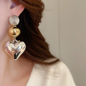 Detailed shot of triple-tier earrings with spiral stud, gold bead, and silver heart charm