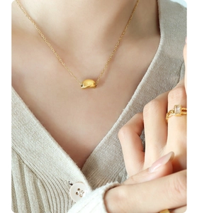 Detail of a minimalist gold bean pendant necklace on a model wearing a beige sweater