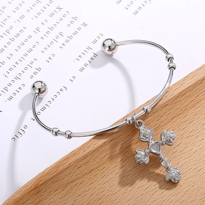 Macro detail of silver cross pendant with rose accents and heart center on open bangle