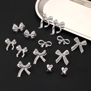 Flat lay of silver stainless steel bow earrings on a gold tray with dark leather