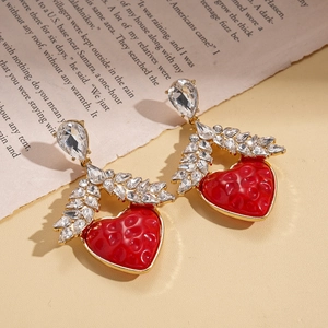 Detail shot of heart-shaped gold drop earrings with red resin and sparkling rhinestones