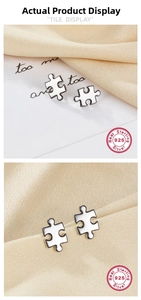Macro view of S925 silver puzzle earrings with white enamel finish on silk fabric