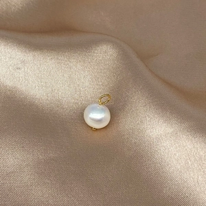 Golden Cuban chain necklace with a single round pearl pendant on champagne silk fabric