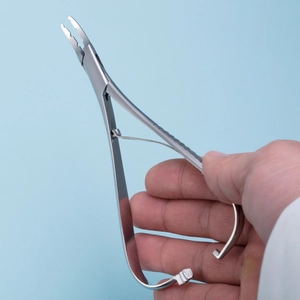 Silberne Piercing-Zange aus Edelstahl in der Hand gehalten auf blauem Hintergrund