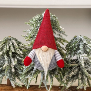 Handmade Christmas gnome hanging ornament with red felt hat and gray beard on snowy pine