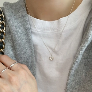 Close-up of minimalist silver heart pendant necklace and matching ring on model