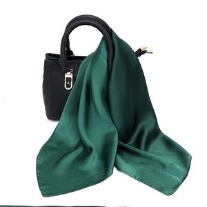 Detail view of dark green silk satin scarf draped over a black textured leather handbag