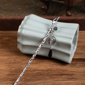 Detailed close-up of a silver metal hair pin with bamboo texture and tassel pendant