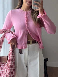 Detail of pink knitted cardigan featuring elegant ruffled edges on the button placket and cuffs