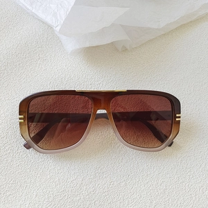 Detail of oval sunglasses with brown gradient lenses and gold metal hinge accents