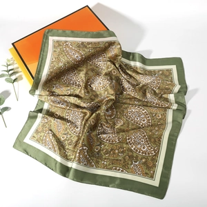 Detailed view of paisley silk square scarf with olive green border near orange gift box