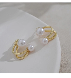 Detail of gold curved pearl earrings on a minimalist cream ceramic tray background