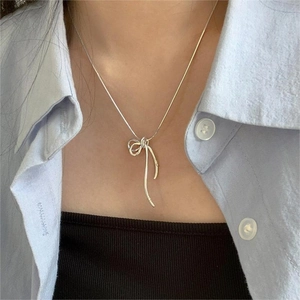 Close-up of silver bow pendant on a delicate snake chain necklace worn on neck