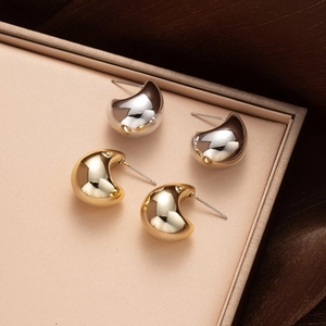 Macro detail of glossy gold and silver teardrop stud earrings on soft silk background