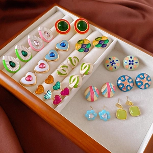 Macro view of colorful enamel flower and heart earrings in a vintage wooden jewelry box