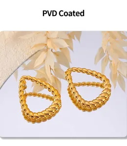 Close-up of golden PVD coated twisted hoop earrings reflecting on a mirror surface