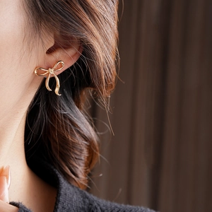 Gros plan d'une boucle d'oreille nœud dorée portée par un mannequin, fini poli