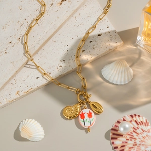 Détail d'un collier doré avec pendentif tulipe sur marbre entouré de coquillages