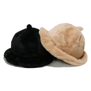 Detail view of plush faux fur bucket hats in black and beige showing soft texture and pom-pom