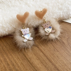 Detail of velvet heart stud earring with golden bear pendant and fluffy fur pompom charm