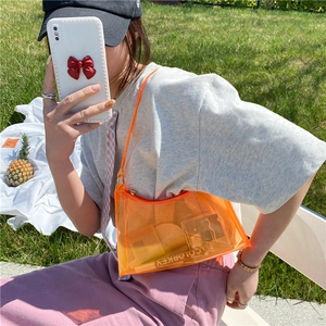 Outdoor shot of stylish orange transparent PVC baguette bag for women on sunny grass