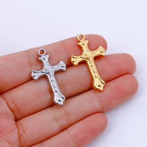 Macro view of gold and silver layered crucifix pendants held in hand for size contrast