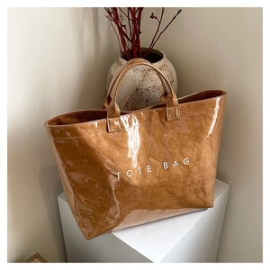 Detail of a brown glossy tote bag with TOTE BAG print on a minimalist pedestal