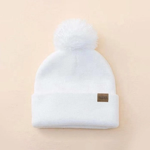 Detailed close-up of a white knit beanie with soft pompom and FASHION leather patch