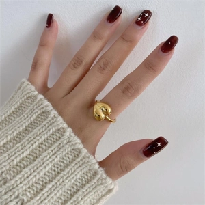 Close-up of a heart-shaped gold ring in sterling silver worn on a finger with red nails