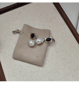 Dettaglio orecchini con perle barocche e pietra nera su base dorata e sacchetto beige