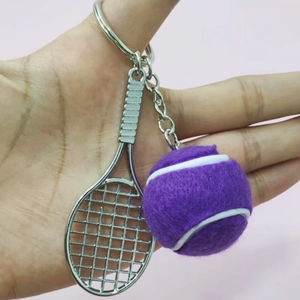 Macro view of silver tennis racket and purple felt ball keychain held by hand