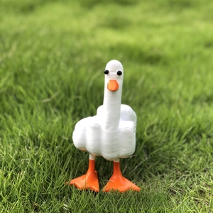 Detailed view of creative white resin duck statue with middle finger gesture on grass