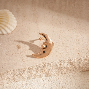 Detail of gold crescent moon face ear cuff on beige stone with coastal shell decor