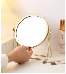 Detail of round gold iron frame vanity mirror being held showing stable metal base