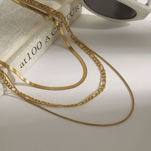 Three-layer gold stacked necklace featuring snake and figaro chains on white background