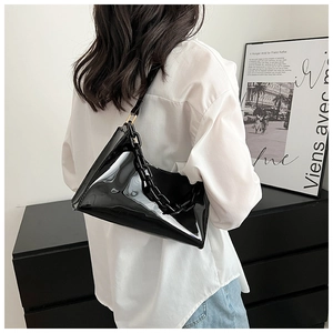 Detail of a black glossy patent leather shoulder bag with a sleek chain handle on a model