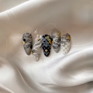 Detail of artistic press-on nails featuring grey wave patterns and gold bead accents
