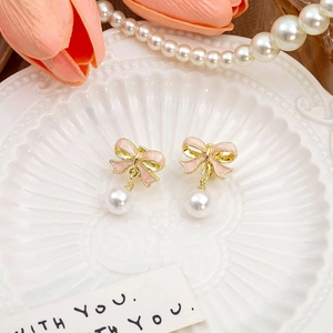 Macro shot of pink enamel bow earrings with white round pearl drops on a white plate