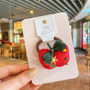 Gros plan sur un élastique à cheveux pomme rouge en peluche avec nœud vert et sequins