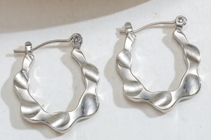 Detail of silver geometric earrings with irregular wave texture and polished steel finish