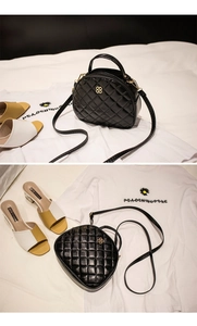 Detail of black quilted crossbody bag featuring gold-tone clover logo and chain strap