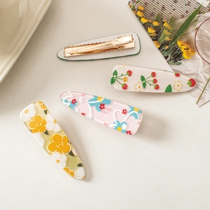 Detail of four colorful acrylic flower and strawberry hair clips on a beige surface
