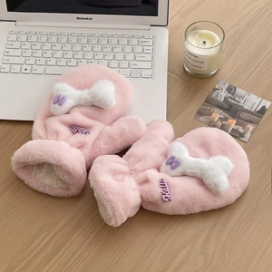 Close-up of pink plush mittens with white bone pom-poms and hello embroidery on wood