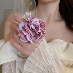 Detailaufnahme eines rosa Seidenblumenrings an einer Hand, die ein Glas hält