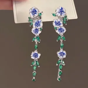 Blue and white floral drop earrings with green zircon leaves on a display card