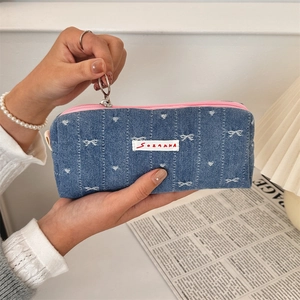 Close-up of denim pencil case with white bow pattern and contrasting pink zipper detail