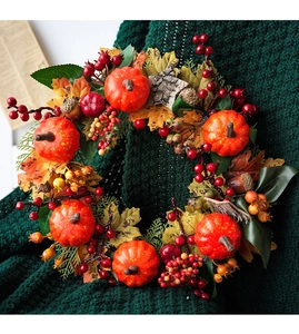 Close-up of fall wreath featuring orange pumpkins, red berries, and autumn maple leaves
